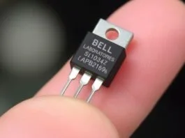 A close-up photograph of a vintage Bell Laboratories point-contact transistor, a significant milestone in the History of Processors, highlighting its small size compared to a human finger.