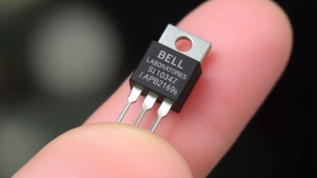 A close-up photograph of a vintage Bell Laboratories point-contact transistor, a significant milestone in the History of Processors, highlighting its small size compared to a human finger.