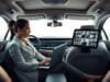 eSIM Mobile Office: Your Car’s Ultimate Workspace A professional woman working on a laptop in a modern car's back seat, creating an efficient eSIM mobile office, with a tablet mounted on the dashboard showing a video conference.