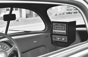 History of mobile phones: How the Transformed Our World An old black and white photo of a 1940s car with a large, boxy radio telephone receiver on the dashboard, illustrating the early history of mobile phones.