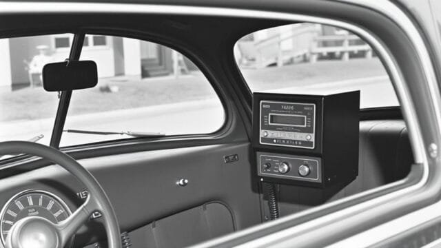 History of mobile phones: How the Transformed Our World An old black and white photo of a 1940s car with a large, boxy radio telephone receiver on the dashboard, illustrating the early history of mobile phones.